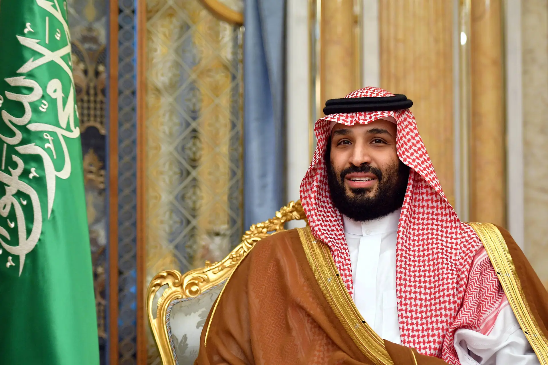 O presidente da Arábia Saudita sentado em uma cadeira, com a bandeira da Arábia Saudita ao fundo