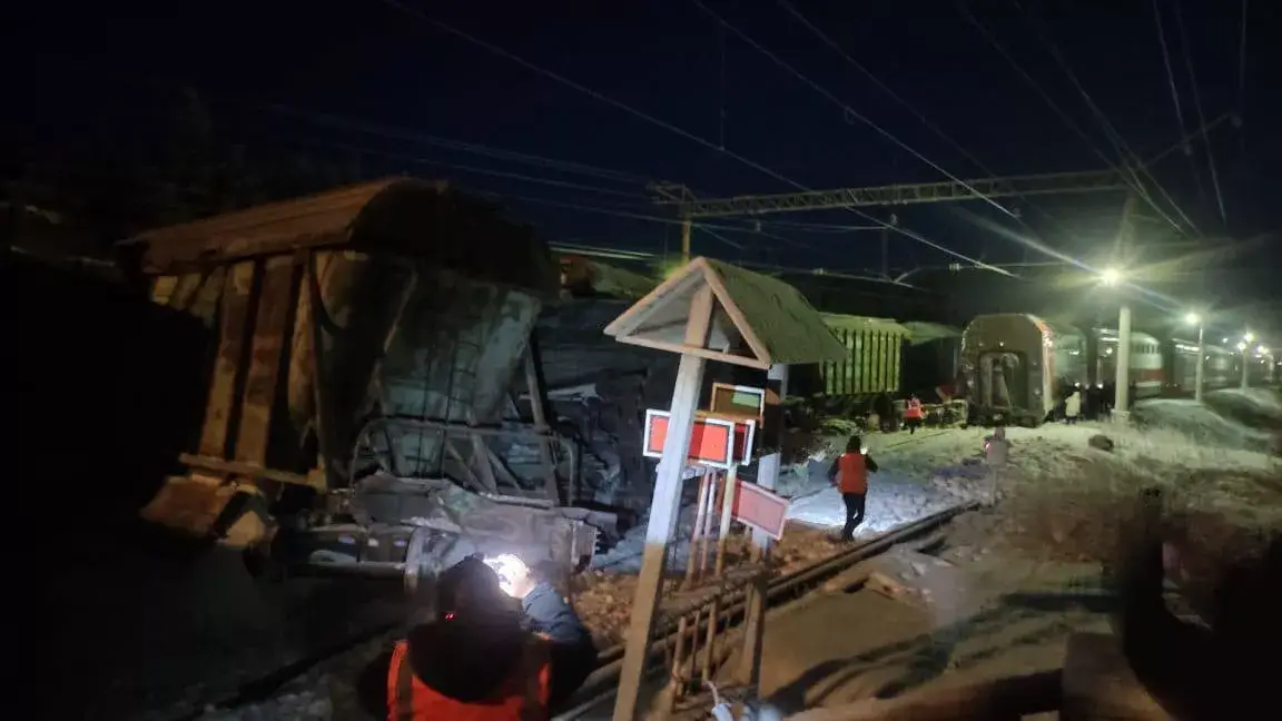 Trabalhadores de resgate com roupas laranjas e lanternas se aproximando do trem descarrilado à noite na estação de Knyazhaya, Rússia.