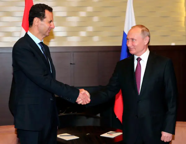 Vladimir Putin apertando as mãos de Bashar al-Assad durante uma reunião diplomática, simbolizando o apoio russo ao regime sírio.