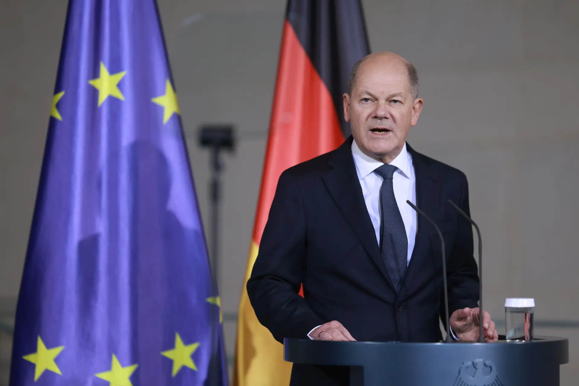 Chanceler alemão Scholz discursando com bandeiras da Alemanha e da UE ao fundo, destacando a independência das eleições.