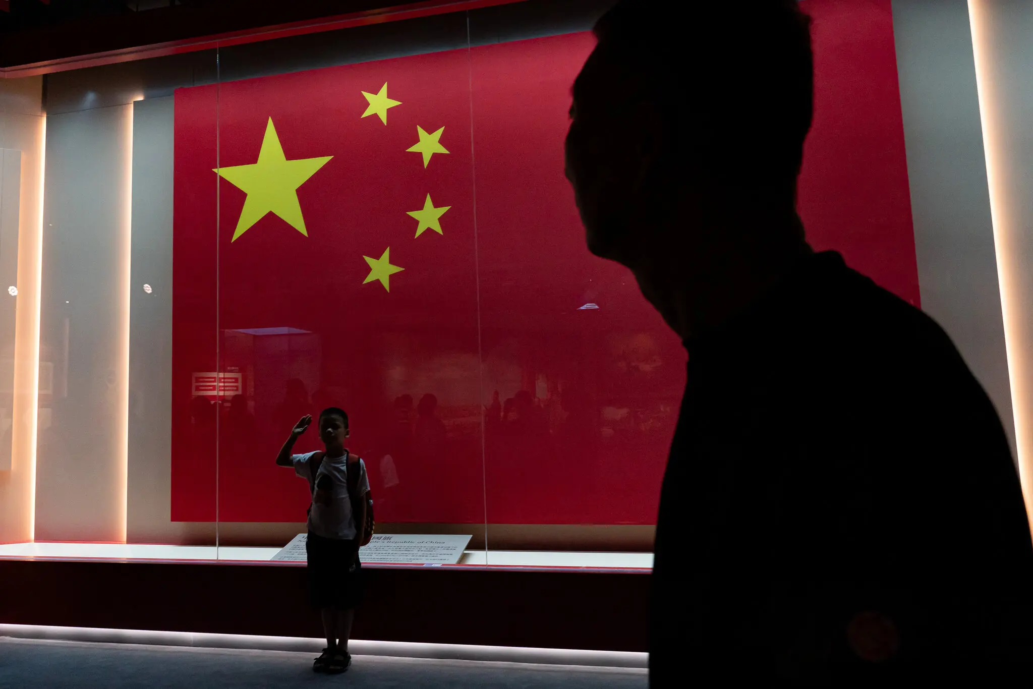 Sombra de um homem e um menino fazendo o símbolo do exército com a bandeira da China ao fundo.