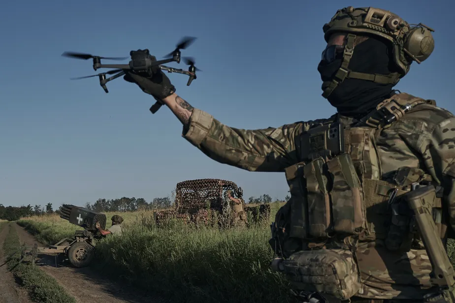 Soldado russo observando um drone no céu enquanto monitora a área, simbolizando a ameaça dos ataques aéreos em solo russo.