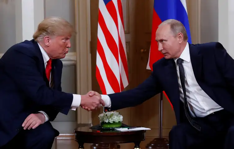 Vladimir Putin e Donald Trump apertam as mãos em uma reunião formal, com as bandeiras dos Estados Unidos e da Rússia ao fundo, simbolizando a reaproximação diplomática entre os dois países.