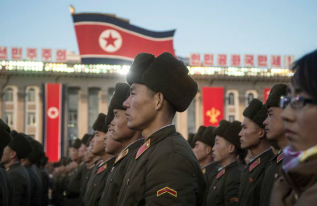 Soldado da Coreia do Norte com a bandeira nacional ao fundo, simbolizando a pressão e os desafios enfrentados pelos soldados norte-coreanos enviados para combater na guerra contra a Ucrânia.