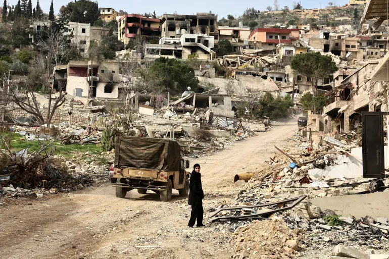 Um residente retornando caminha perto de um local danificado em meio a prédios destruídos, enquanto as tropas israelenses se retiraram da maior parte do sul do Líbano, na vila de Kfar Kila, no sul do Líbano [Emilie Madi/Reuters]. Fonte: Al Jazeera