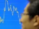 Homem passa em frente a um gráfico que mostra a oscilação do Índice Hang Seng em Hong Kong.