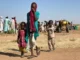 Mulher sudanesa deslocada, acompanhada de crianças, caminha em um campo de refugiados perto da cidade de Tawila, em Darfur do Norte, em 11 de fevereiro de 2025, durante a guerra em andamento entre o exército e as forças paramilitares.