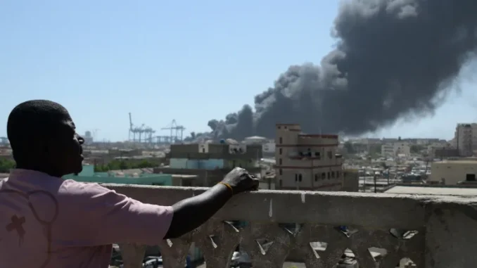 AFP__20250506__44LG3KD__v2__HighRes__TopshotSudanConflict-1746520535 Homem observa a fumaça após ataque de drone em Port Sudan
