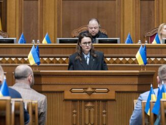Yulia Svyrydenko discursando no Parlamento ucraniano durante a sessão de reformulação do governo, com bandeiras da Ucrânia e da União Europeia ao fundo.