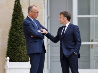 Presidente francês Emmanuel Macron conversando de forma séria com o chanceler alemão Friedrich Merz em frente a um edifício oficial, ambos vestidos com ternos escuros.