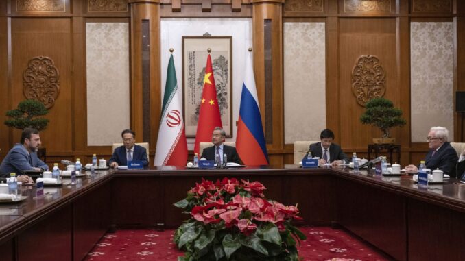 Reunião diplomática trilateral entre China, Irã e Rússia com representantes sentados à mesa e bandeiras nacionais ao fundo.