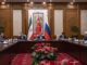 Reunião diplomática trilateral entre China, Irã e Rússia com representantes sentados à mesa e bandeiras nacionais ao fundo.