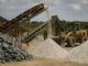 Imagem de uma pedreira na África com equipamentos industriais de mineração, mostrando pilhas de minerais e um trabalhador usando capacete de segurança ao fundo.