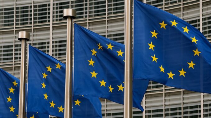Comissão Europeia Propõe Novo Orçamento Plurianual com Ênfase em Defesa, Segurança e Prioridades Emergentes Bandeiras da União Europeia tremulando ao vento em frente a um edifício moderno com janelas de vidro.