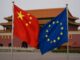 Bandeiras da China e da União Europeia tremulando em frente a um edifício tradicional chinês em Pequim.