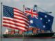 Bandeiras dos Estados Unidos e da Austrália tremulando juntas em um porto com navio cargueiro ao fundo.
