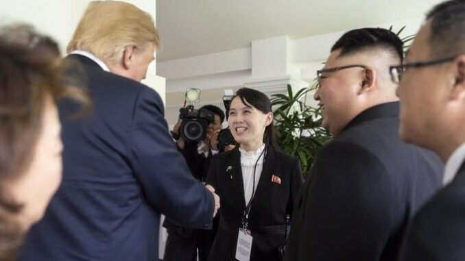 Kim Yo Jong em encontro histórico com Donald Trump e Kim Jong-un Kim Yo Jong sorrindo e cumprimentando Donald Trump durante reunião, com Kim Jong-un ao lado.