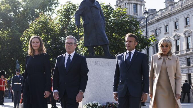 Keir Starmer e sua esposa ao lado de Emmanuel Macron e Brigitte Macron caminhando próximos à estátua de Winston Churchill em Londres, em um dia ensolarado.