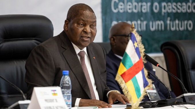 Touadéra anuncia candidatura em meio a desafios da República Centro-Africana Presidente Faustin-Archange Touadéra da República Centro-Africana discursando em evento oficial, com a bandeira nacional em destaque à frente.