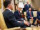 Foto de Donald Trump e outros políticos em uma reunião formal, com Trump sentado no centro olhando seriamente para um interlocutor.