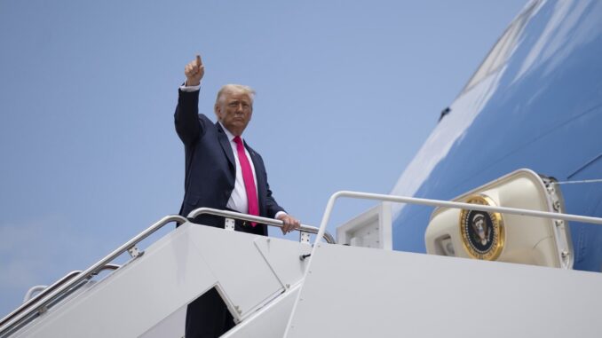 Gv7AczJXYAAemQD Donald Trump acenando com o polegar para cima ao embarcar em avião presidencial sob céu azul claro.