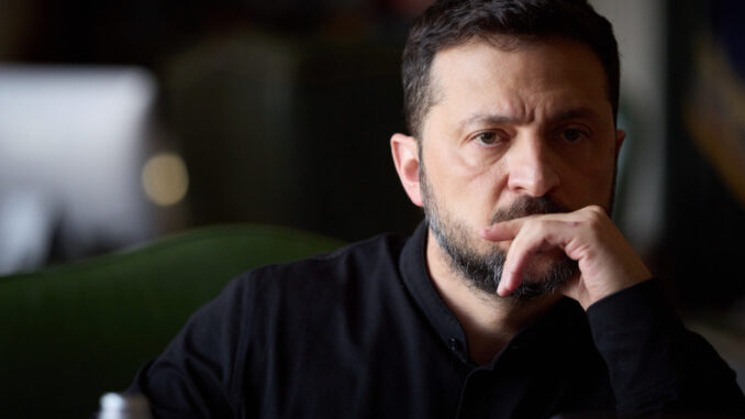 Retrato do presidente ucraniano Volodymyr Zelensky, com expressão pensativa, vestindo camisa preta, em ambiente com iluminação suave e fundo desfocado.