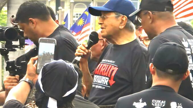 Mahathir Mohamad lidera protesto #TurunAnwar em Kuala Lumpur Ex-primeiro-ministro malaio Dr. Mahathir Mohamad discursando em protesto #TurunAnwar na Praça Merdeka, Kuala Lumpur, cercado por apoiadores com bandeiras da Malásia.