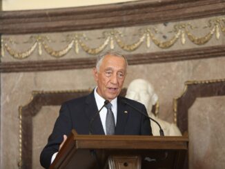Presidente Marcelo Rebelo de Sousa discursando em um púlpito, em ambiente oficial, com estátua ao fundo.