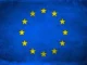 Bandeira da União Europeia azul com estrelas amarelas sobre um fundo claro, simbolizando unidade e cooperação europeia.