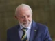 Presidente Luiz Inácio Lula da Silva com terno azul, camisa clara e gravata listrada nas cores verde, amarela e preta, olhando levemente para o lado, com expressão serena. Fundo desfocado.