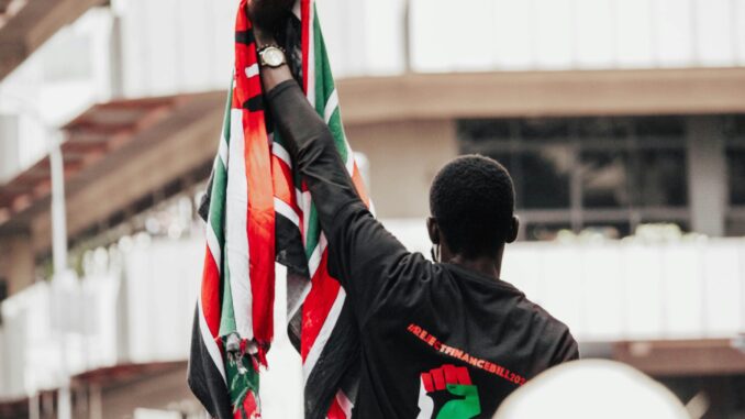 pexels-mcgzay-27719497 Manifestante segurando a bandeira do Quênia durante protesto em Nairóbi.