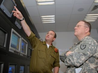 Dois oficiais militares, um israelense e um americano, observam monitores em uma sala de comando durante um briefing estratégico.