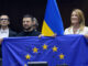 Presidente ucraniano Volodymyr Zelensky e líderes da União Europeia seguram a bandeira da UE durante visita ao Parlamento Europeu.