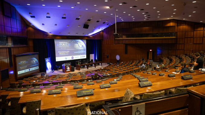 Conferência Nacional do Espaço 2023 – África do Sul Auditório da Conferência Nacional do Espaço 2023 em Pretória, África do Sul, mostrando palco, telões e assentos do público.
