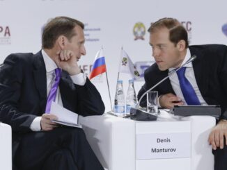 Denis Manturov e outro participante conversando em painel do Fórum Gaidar, com bandeira da Rússia ao fundo.