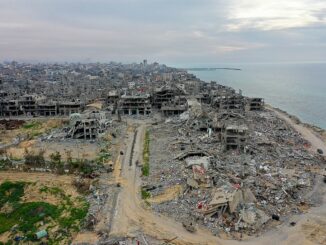 Vista aérea mostrando a destruição causada pelos ataques em Gaza, com edifícios destruídos, destroços e a costa ao fundo.
