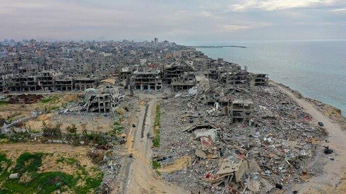 Gaza: Destruição no Campo de Refugiados Vista aérea mostrando a destruição causada pelos ataques em Gaza, com edifícios destruídos, destroços e a costa ao fundo.
