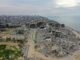 Vista aérea mostrando a destruição causada pelos ataques em Gaza, com edifícios destruídos, destroços e a costa ao fundo.