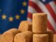 Rolhas de cortiça empilhadas em primeiro plano, com as bandeiras da União Europeia e dos Estados Unidos desfocadas ao fundo.