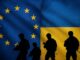Silhuetas de soldados armados diante da fusão das bandeiras da União Europeia e da Ucrânia, simbolizando apoio militar europeu a Kiev.