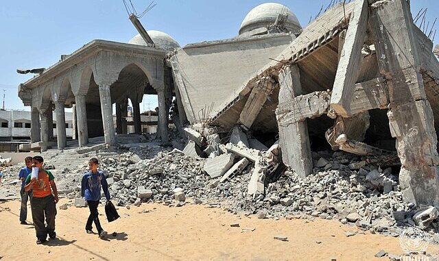 Crianças andando perto de prédios destruídos em Gaza após ataques aéreos, mostrando a devastação urbana e o impacto civil do conflito.