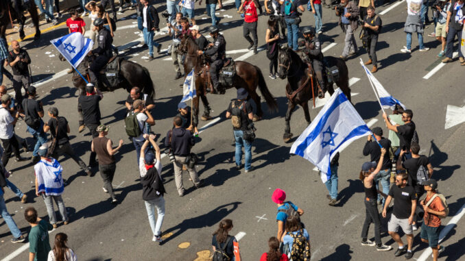 Protestos em Tel Aviv contra a reforma judicial Manifestantes em Tel Aviv bloqueiam uma rodovia durante protestos contra a reforma judicial de Israel, enquanto policiais montados tentam controlar a multidão.