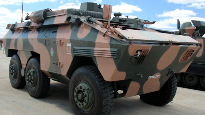 Blindado EE-11 Urutu: Símbolo da Defesa Brasileira e Cooperação Regional Veículo blindado EE-11 Urutu com camuflagem verde e marrom estacionado em área externa, sob céu azul com nuvens.
