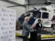 Senador Roger Wicker falando em um púlpito com logotipo da UMMC, com um helicóptero AirCare ao fundo e fotógrafos registrando o evento.