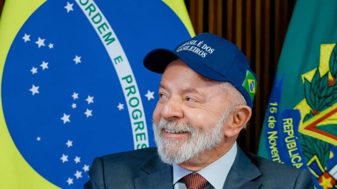 Presidente Lula sorrindo em evento oficial Presidente Luiz Inácio Lula da Silva usando boné azul com a frase "O Brasil é dos brasileiros", sorrindo, com a bandeira do Brasil ao fundo.