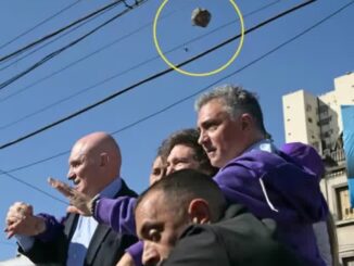 Presidente argentino Javier Milei em carreata, com segurança próxima, enquanto um objeto é arremessado do alto em sua direção.
