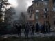 Pessoas observam bombeiros trabalhando enquanto fumaça sai de um prédio residencial danificado em Kiev após ataque com mísseis russos.