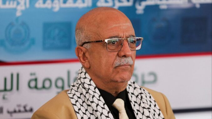 ahmed-al-rahawi-houthi-iemen Foto do primeiro-ministro houthi Ahmed Ghaleb al-Rahawi usando óculos, gravata e lenço palestino, em evento oficial em Sanaa, Iémen.