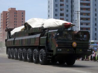 Míssil balístico norte-coreano coberto sendo transportado em caminhão durante desfile militar em cidade urbana.