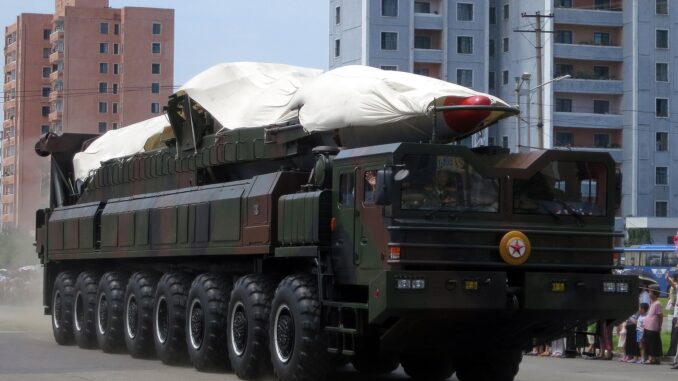 Míssil balístico norte-coreano coberto sendo transportado em caminhão durante desfile militar em cidade urbana.